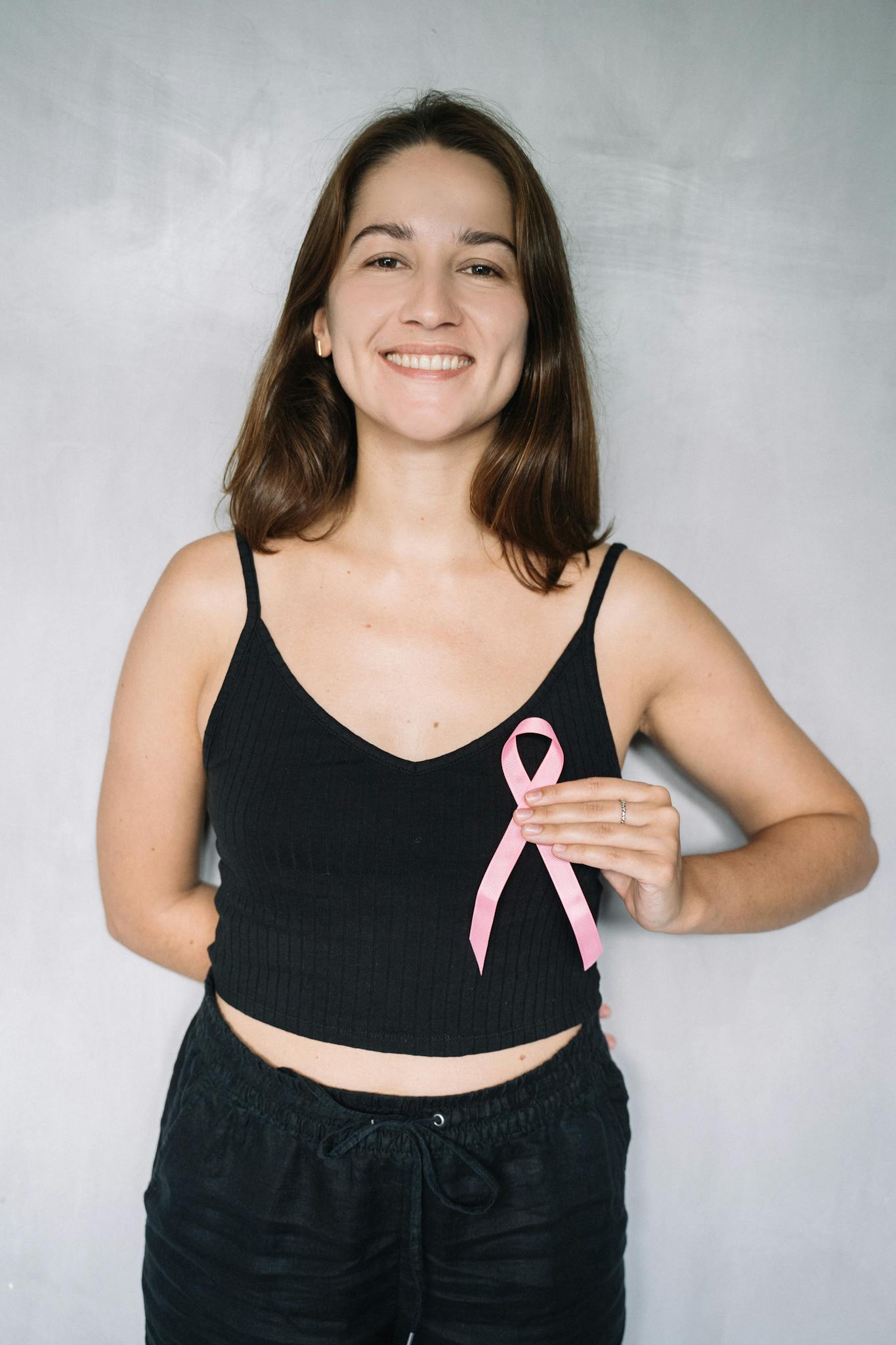 Smiling woman holding a pink ribbon for breast cancer awareness.