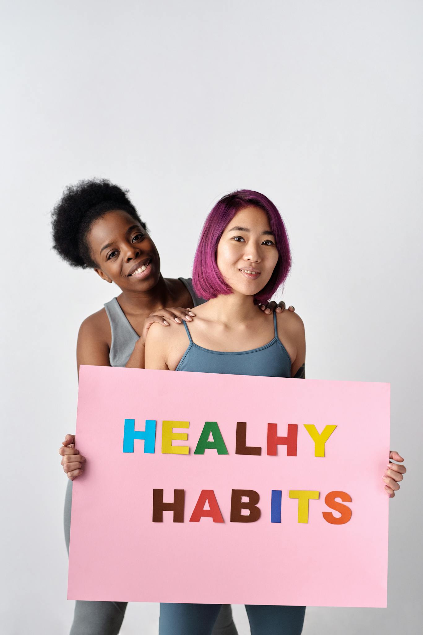Two diverse women holding a healthy habits sign, promoting wellness.